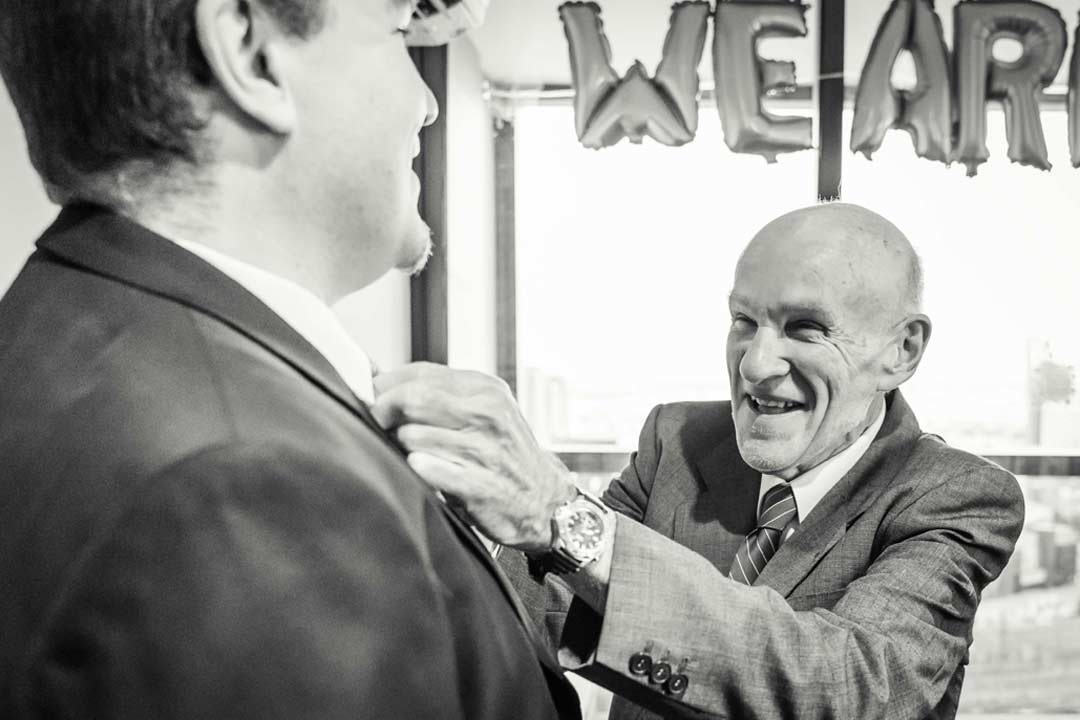 emotional image of father helping son put his tie on captured by wedding photographer Black Avenue Productions in Dockland Melbourne