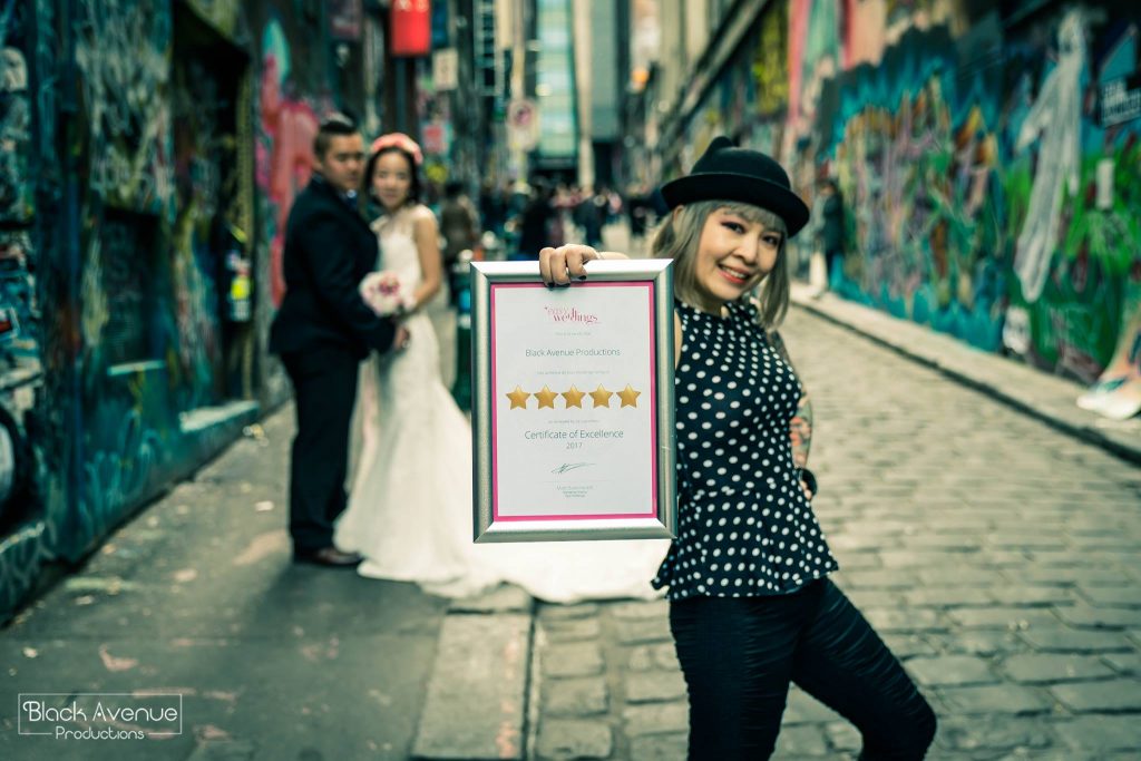 Proud female photographer holding a 5 star award winning frame by Easy Weddings posing in front of just married couple in CBD graffiti lane