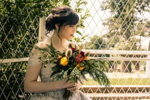 beautiful bride in her latte colour full bridal gown from Leah S Design holding a bunch of trendy forest wheat grass flower bouquet sitting in Overnewton Castle captured by Black Avenue Productions