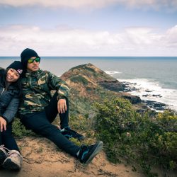 cool couple sat down by the mountain hill top for their professional engagement photography session in Australia by the ocean