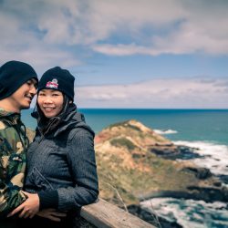 sweet couple hug each other on mountain top smiling for Melbourne wedding photographer Black Avenue Productions with ocean and wave background in 2017
