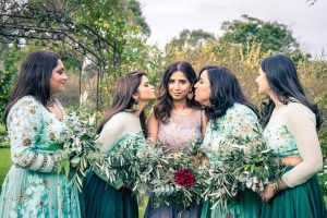 bridal party photo inspiration of bridesmaids kissing the bride in the middle holding on woodland greenery wedding setting