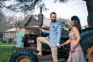 playful groom taking bride to an old farmhouse wagon for their wedding photo in Baxter Barn