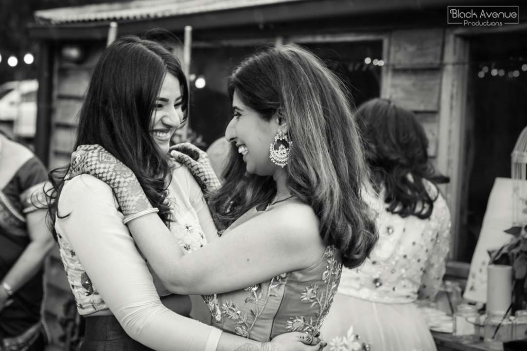 emotional black and white image showing two best friends hugging celebrating a rustic greenery barn warehouse wedding capture by Black Avenue Productions
