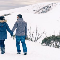 winter engagement photography showing young couple walking in snow mountain hand in hand in ski gear