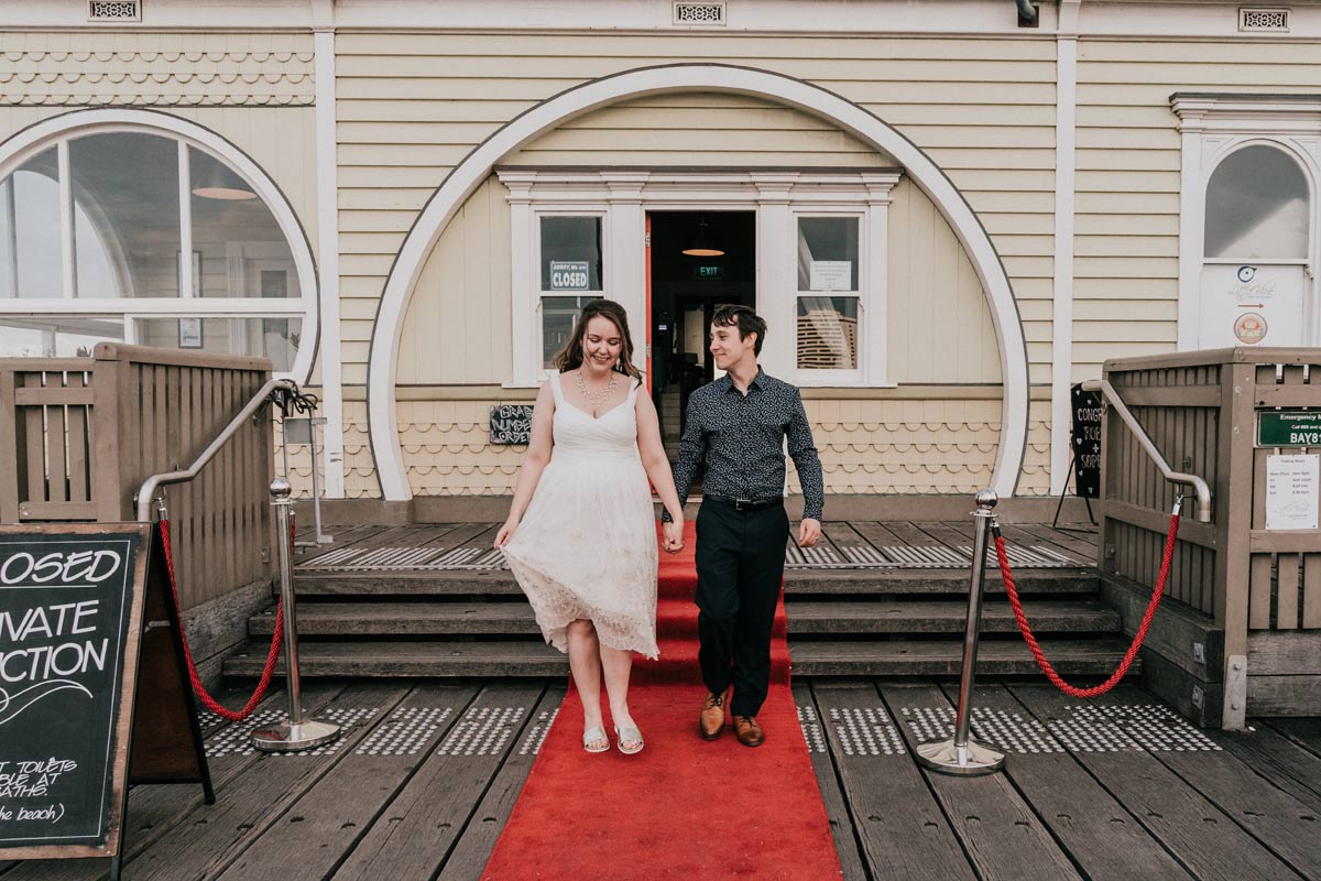 Melbourne bride and groom walking down the aisle of Little Blue Kiosk restaurant in St Kilda pier after wedding ceremony candid shot by wedding videography team from Black Avenue Productions