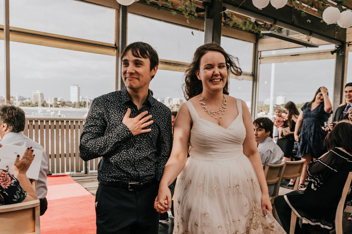 Just married husband and wife walked down the aisle together feeling grateful and joy at Little Blue Kiosk in St Kilda Pier Melbourne captured by candid wedding photographers and videographers team Black Avenue Productions