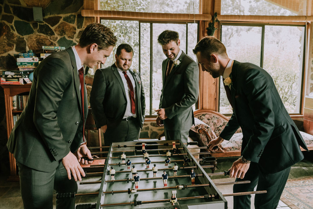 happy groom and groomsmen play football in their rustic farmhouse