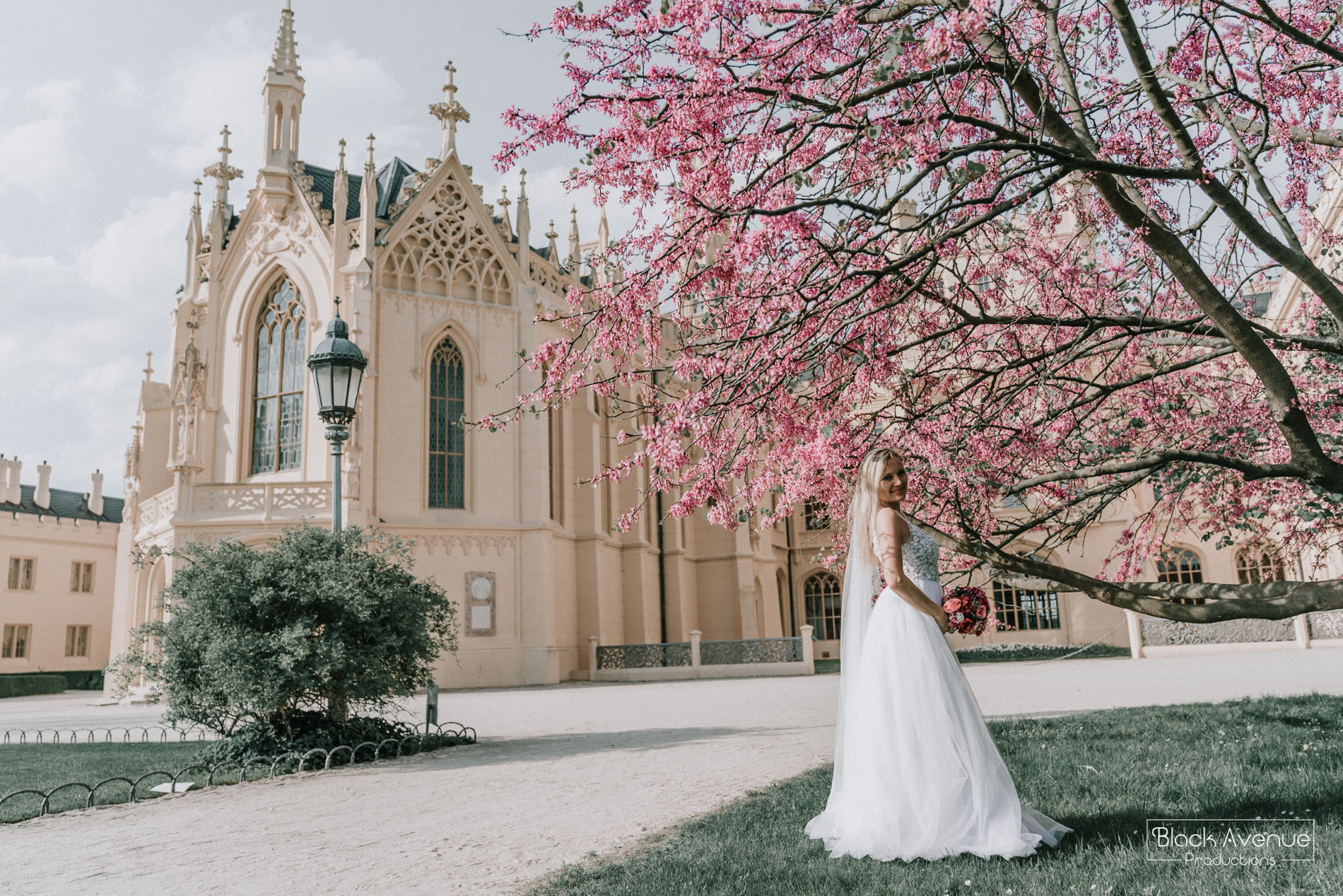 beautiful bride standing under a pink tree in a castle in Europe by destination wedding photographers from Black Avenue Productions