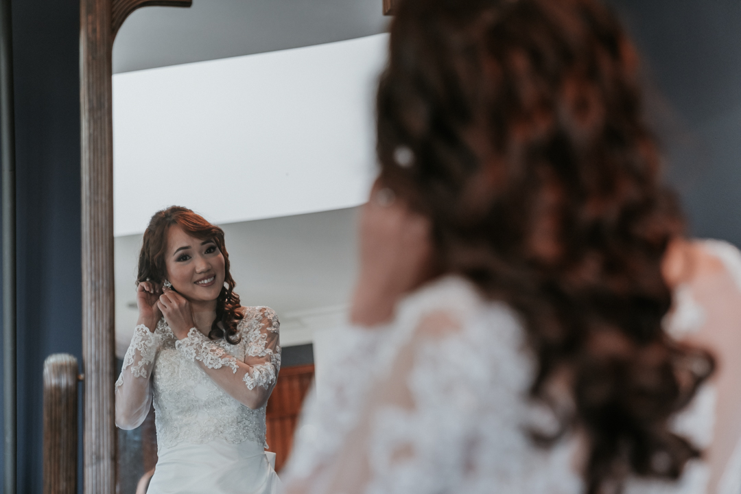 bride looking at mirror put earrings on in her Leah S Design wedding gown at Marybrooke Manor