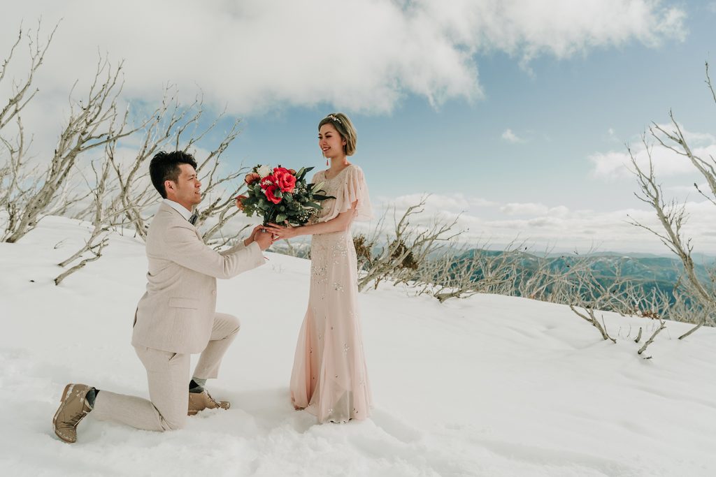 stunning Melbourne couple stood in front of Falls Creek mountain for their snow engagement photos shoot in honest wedding photography style