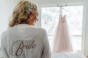 Bride sitting in bed admiring her wedding gown getting ready for her All Smiles beach wedding shortly