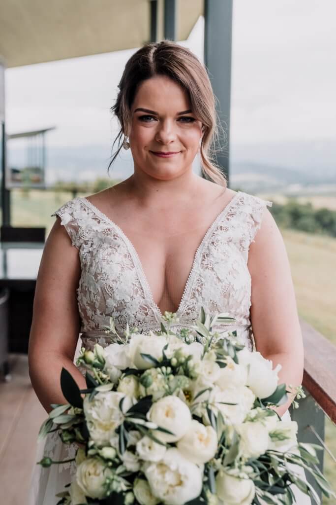 smiling bride wearing a white gown holding white bouquet of roses