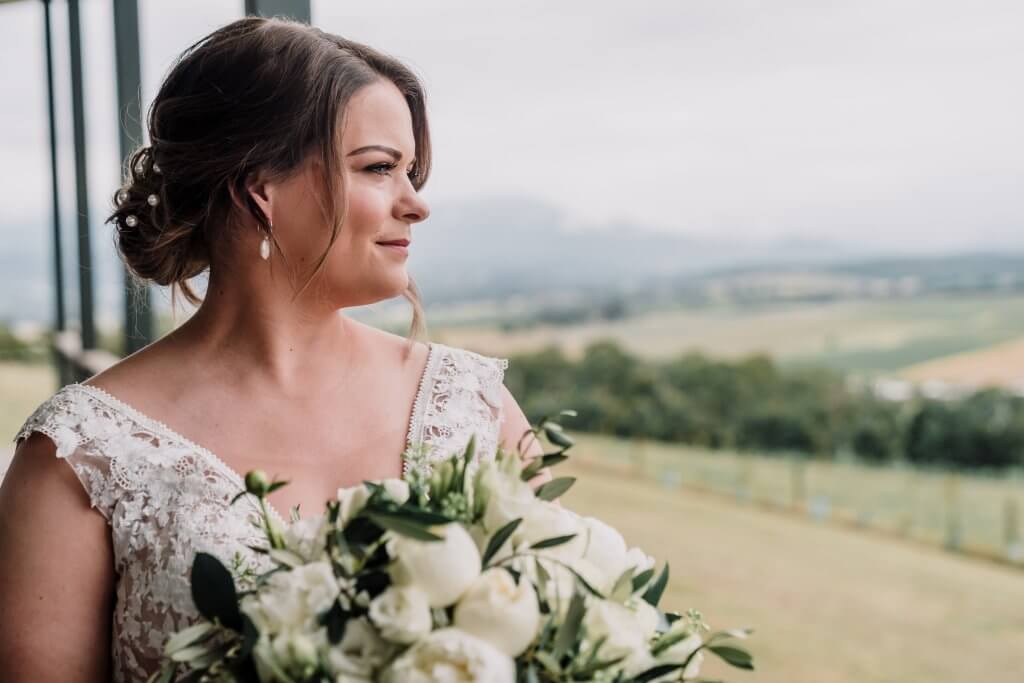 bride looking at the greenfield while holding a bouquet of white roses