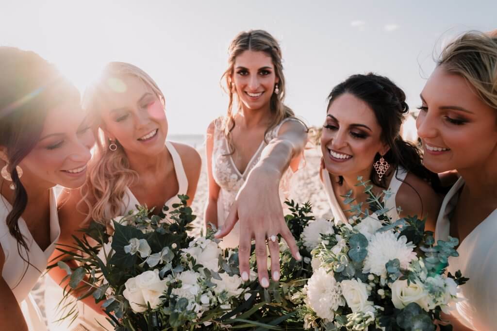 bride showing her ring together with her bridesmaids with flowers under the sunlight