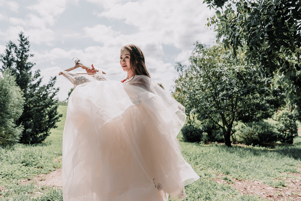 bride holding her wedding gown in a green forrest