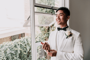asian groom wearing white tuxedo in a magical city wedding in melbourne photo by black avenue productions