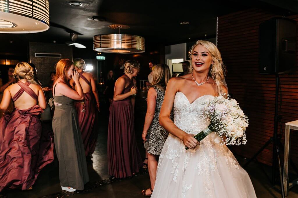 lovely bride posing her lady guests preparing behind her captured by black avenue productions