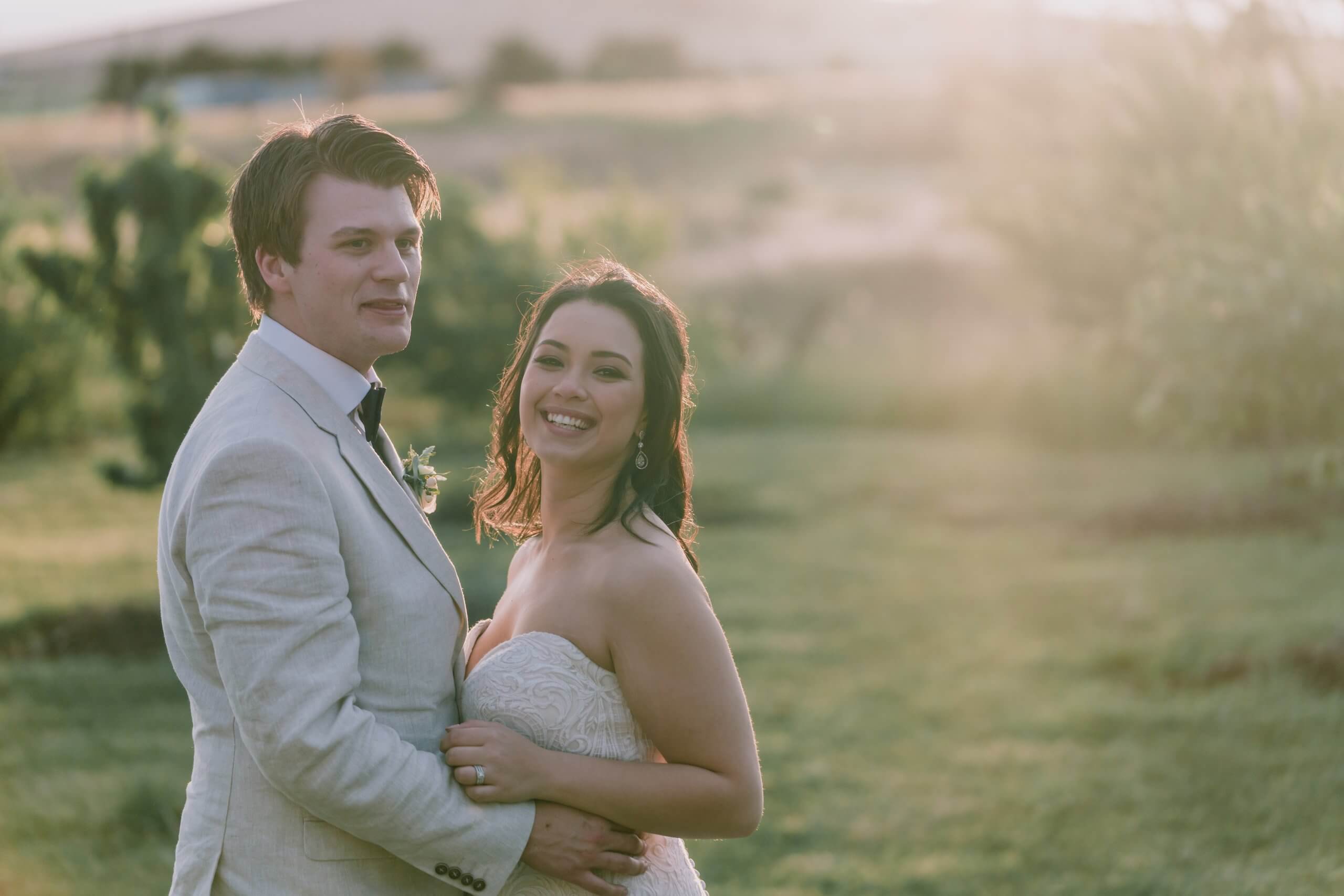 Newlywed Couple Smiling and showing how in love they are by a lovely field, captured by black avenue productions