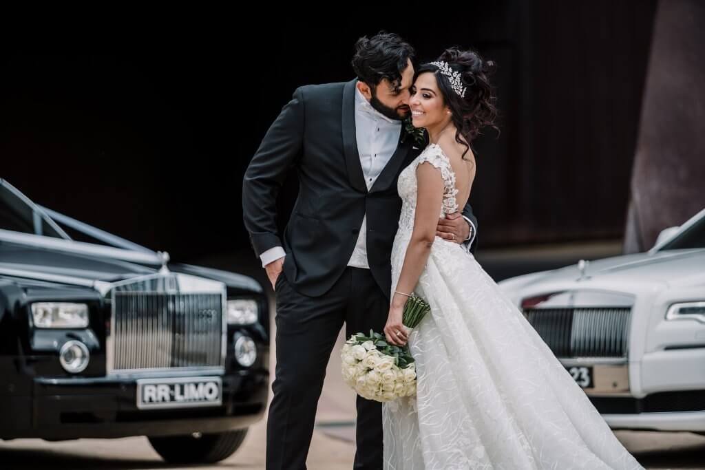 The right suppliers, groom and bride posing in front of 2 luxurious cars that match their suit and gown, captured by Black Avenue Productions
