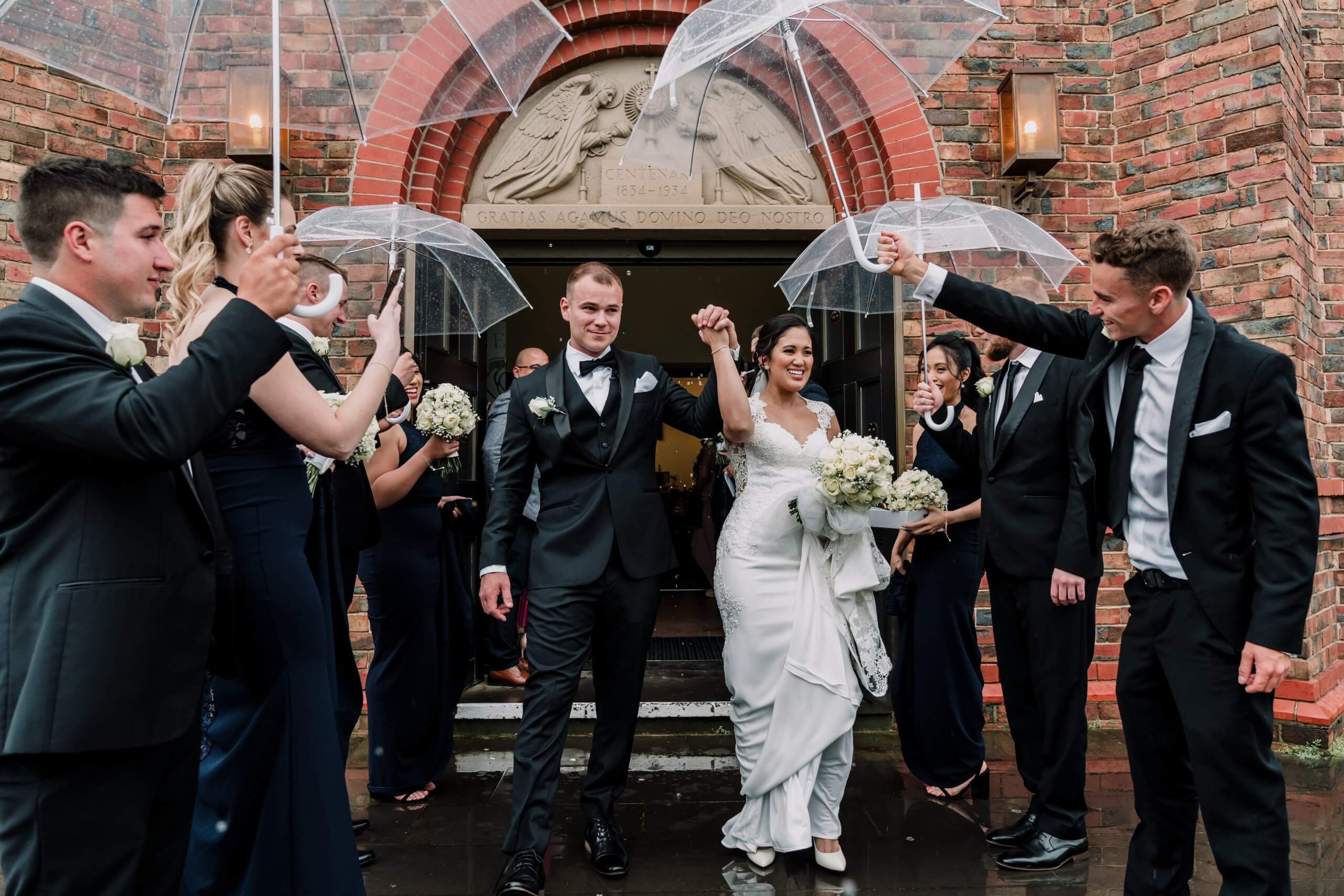 Guests offering umbrellas to the newlyweds while they walk out of the church , captured by black avenue productions. Wedding Day Interrupted by bad weather
