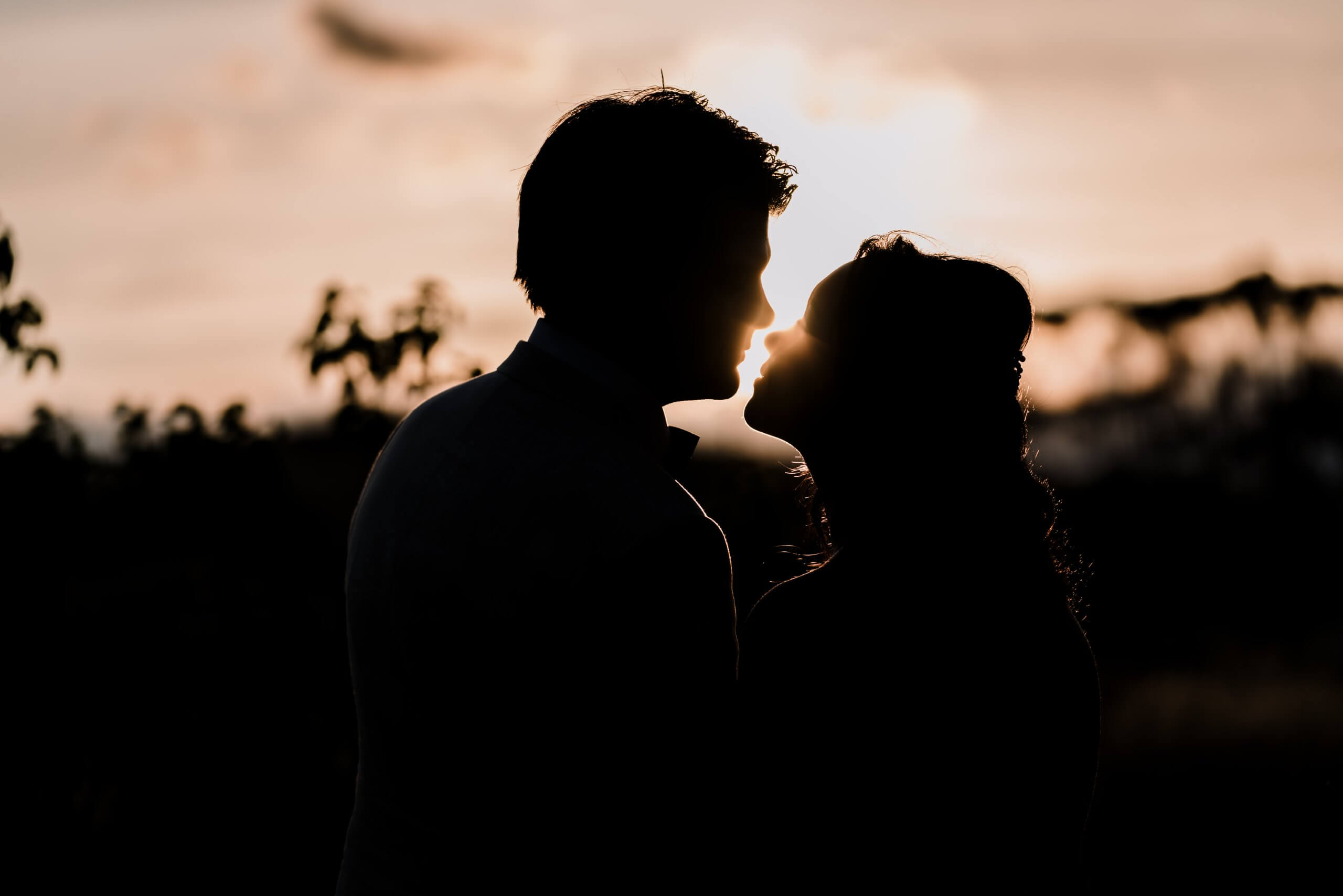 a lovely sunset silhouette shot of the couple almost kissing , captured by black avenue productions
