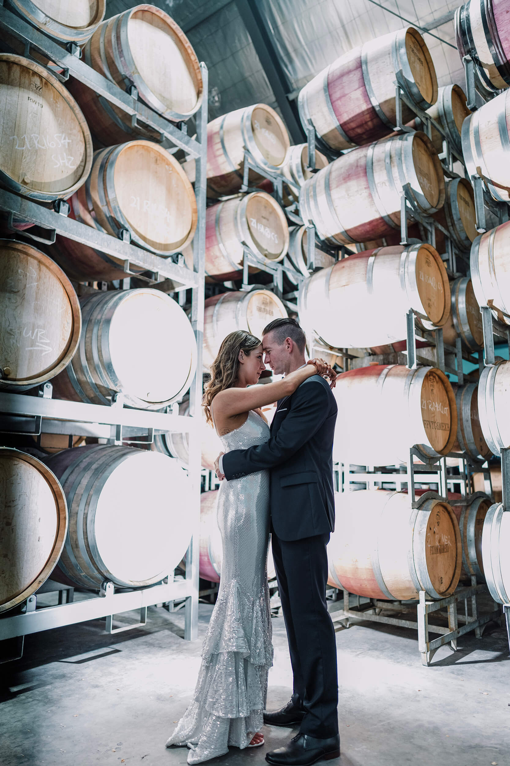 an indoor shot of the bride and groom with the wine barrels stacked up at the background, captured by Derek Chan ofblack avenue productions
