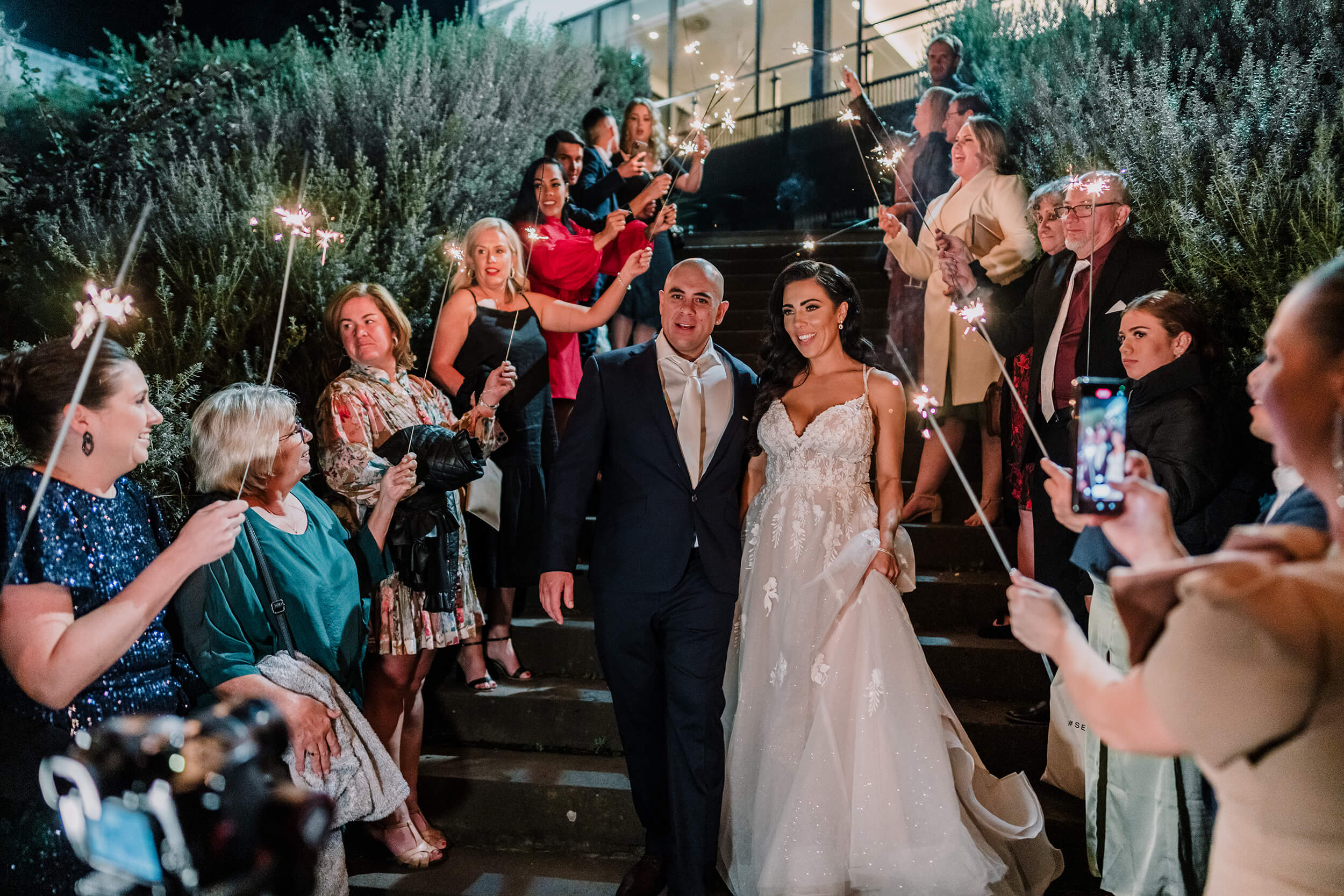 Lovely couple walking down the stairway while guests are holding sparklers, captured by Lowina Blackman of black avenue productions