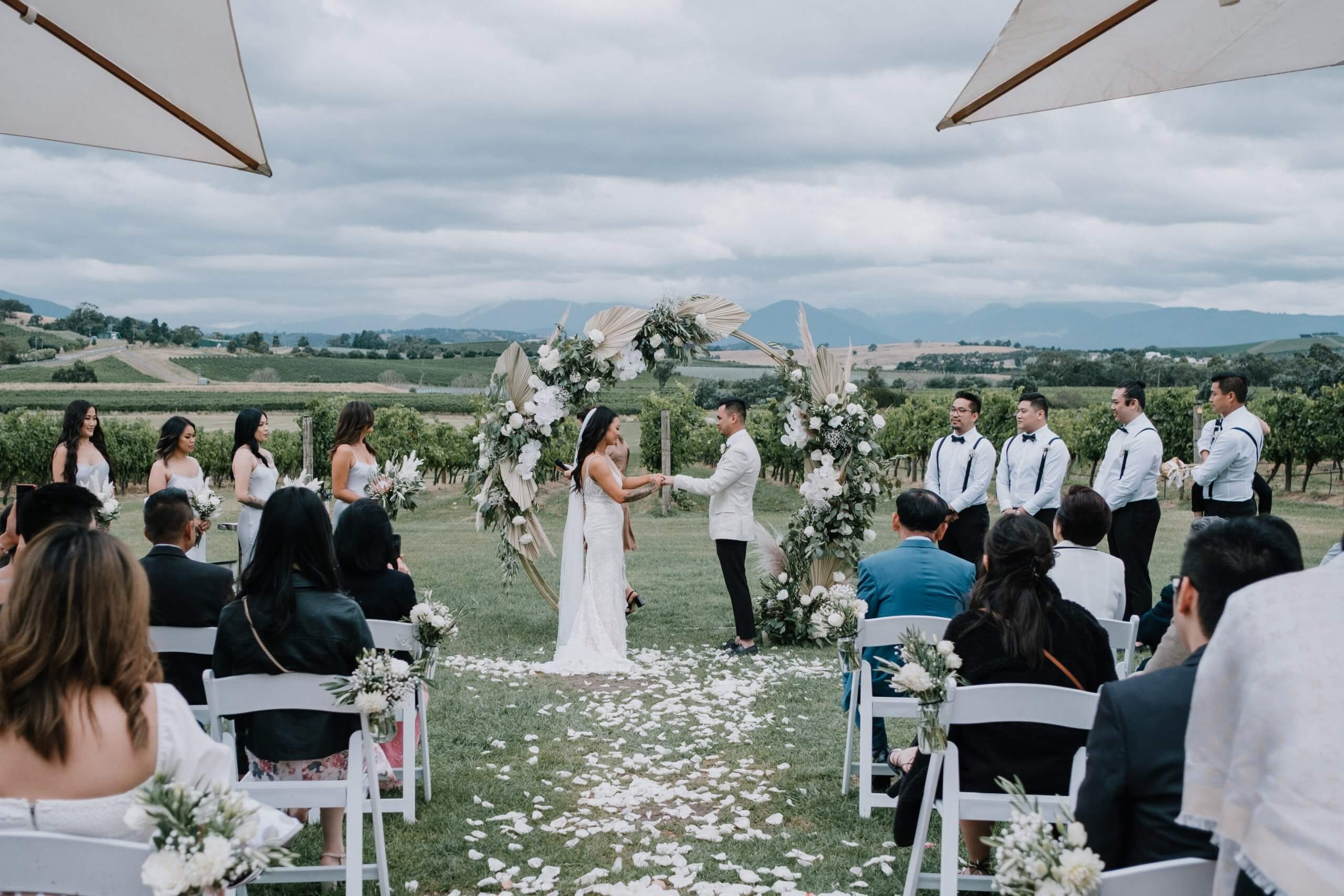 A lovely outdoor wedding ceremony showing the beautiful landscape behind the bride and groom as they are holding each other's hands and saying their vows. Captured by Black Avenue Productions