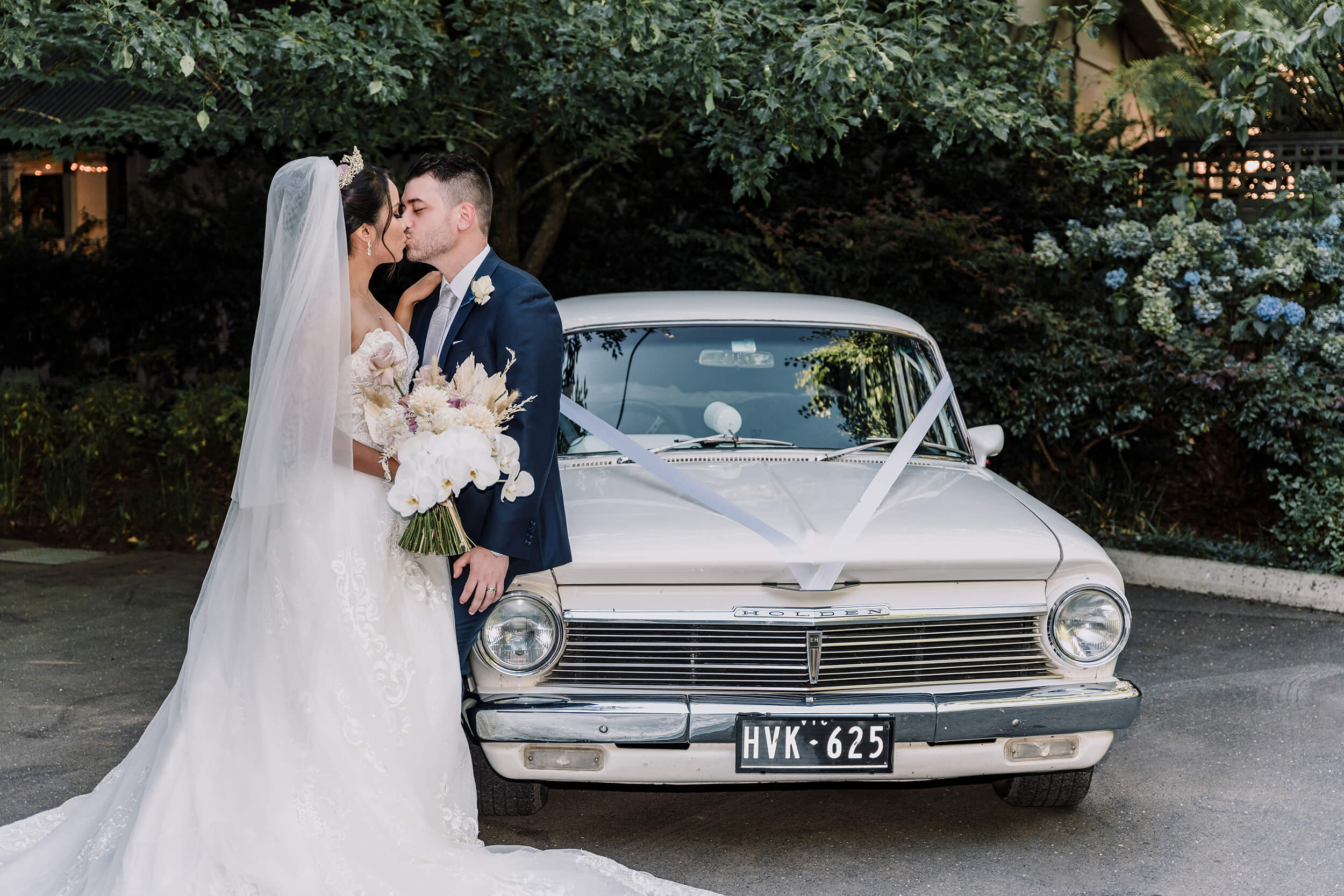 Bride and groom kisses each other by the wedding car. Captured by Black Avenue Productions