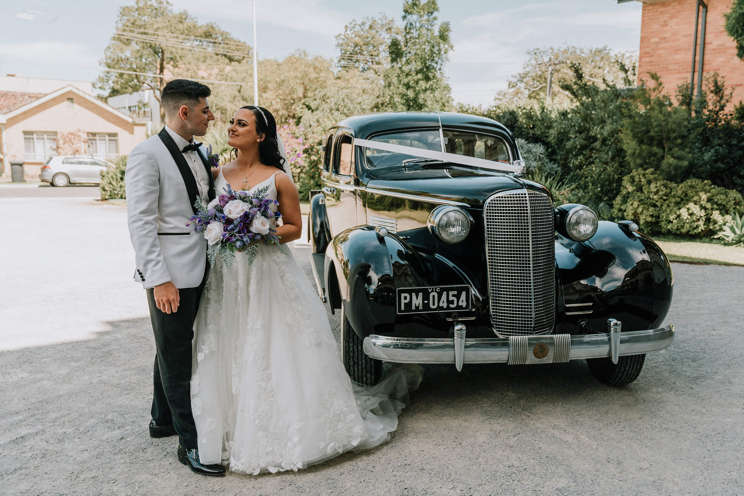 Get a wedding car, Bride and groom happily poses beside a black vintage cadillac. captured by Black Avenue Productions