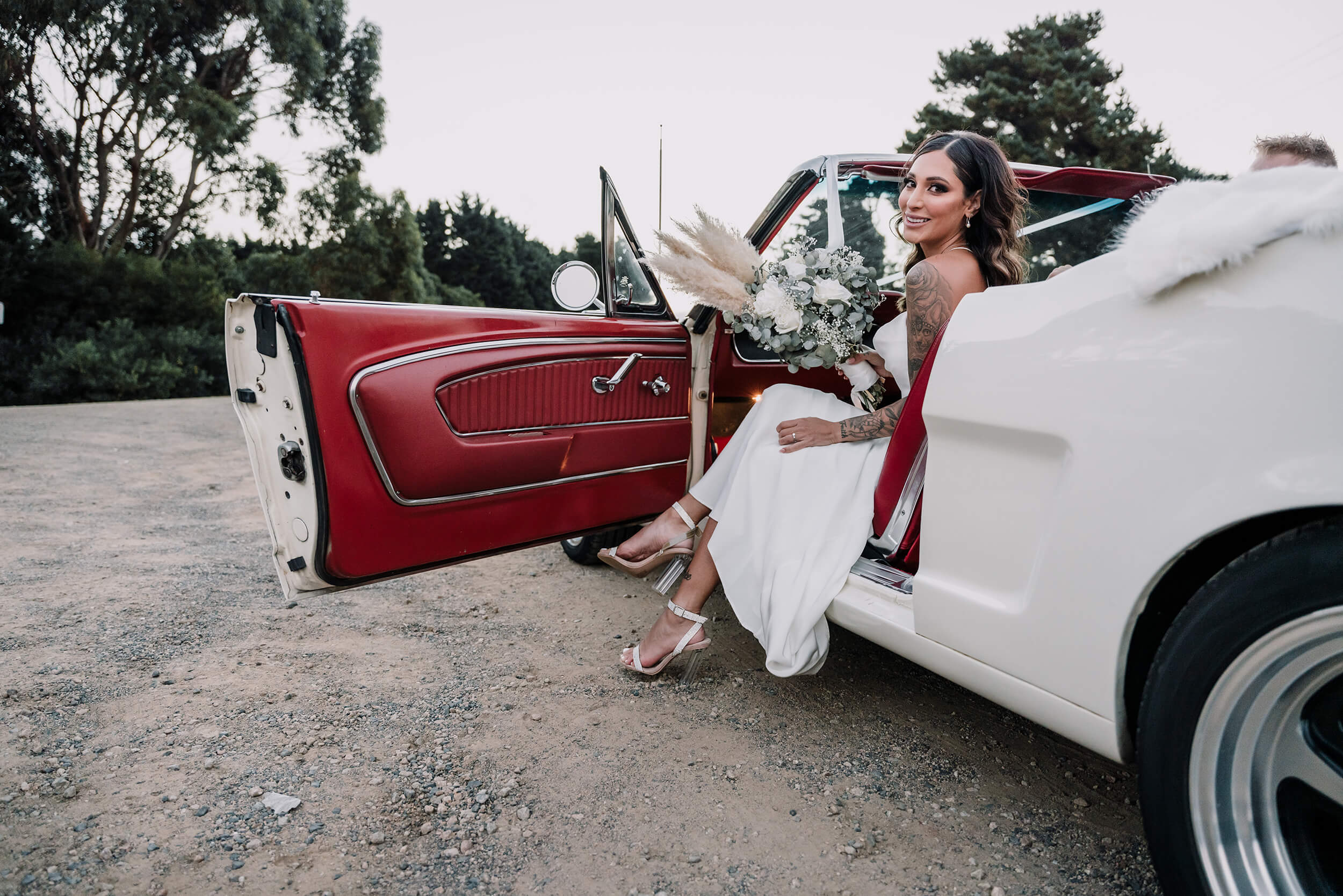 Beautiful bride sitting on an open vintage convertible wedding car, captured by Black Avenue Productions