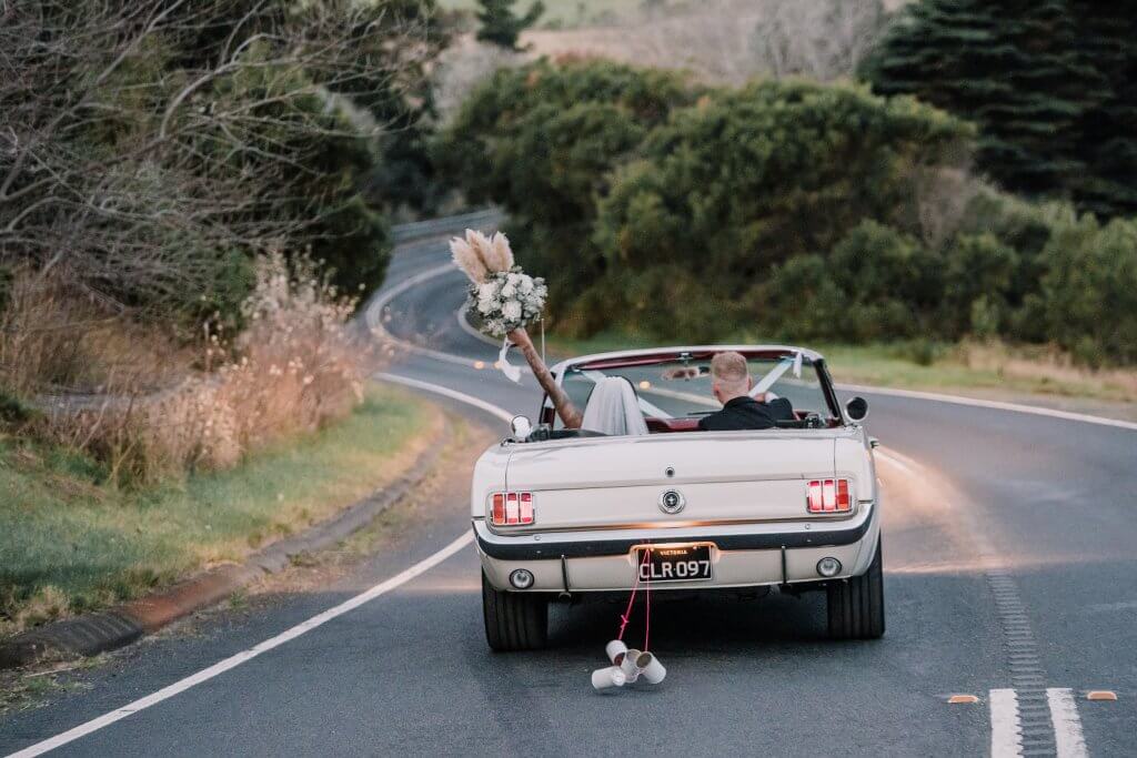 Newly wed couple drives away in a convertible vintage mustang. Captured by Black Avenue Productions
