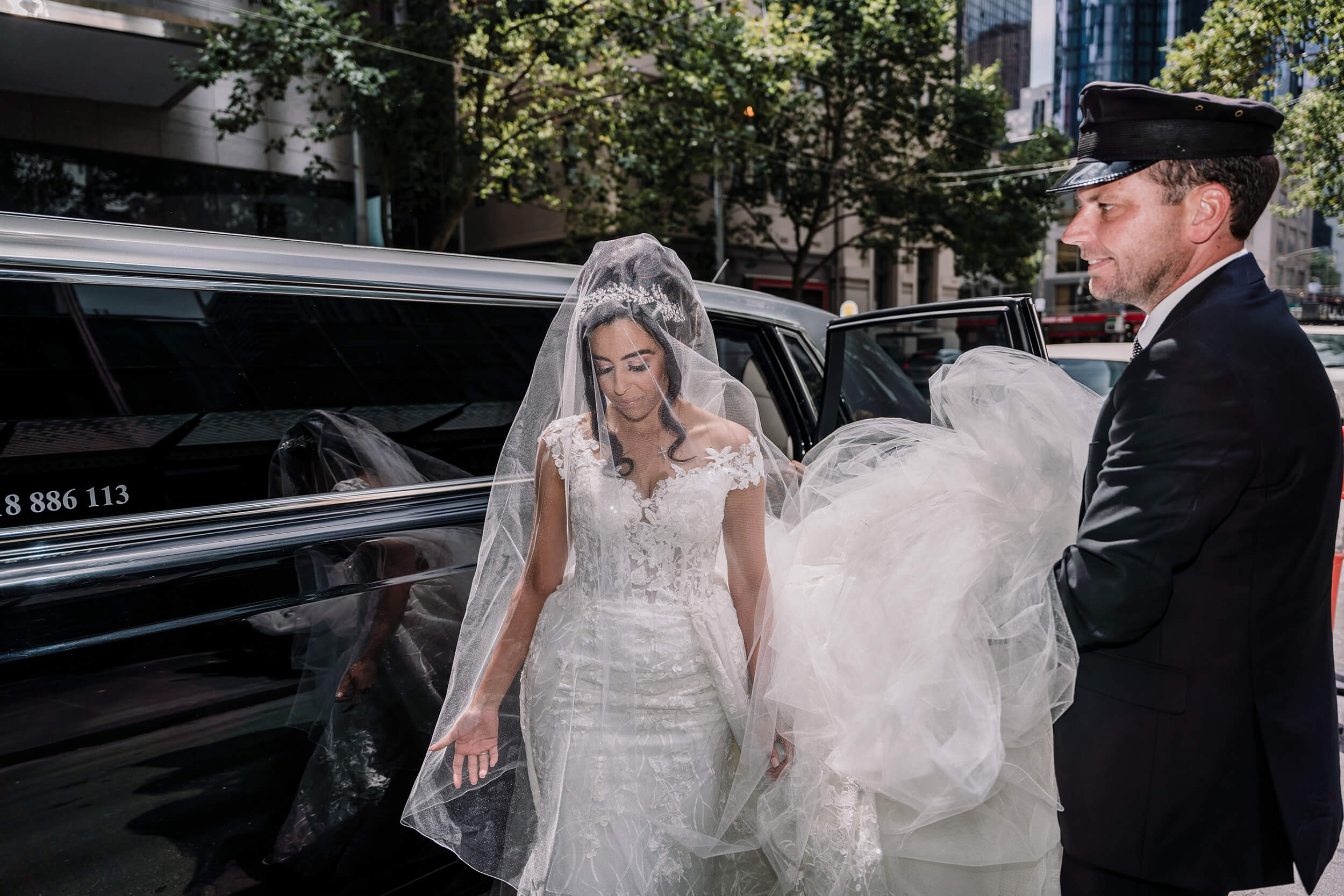 Get a wedding car, bride goes down a luxurious black limousine while the valet holds her veil. Captured by Black Avenue Productions