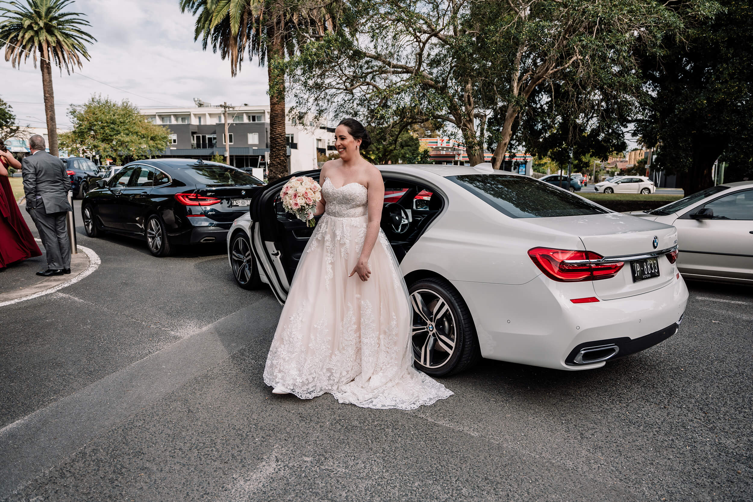 Get a wedding car, bride gets off of a white BMW, smiling and ready to walk down the aisle captured by Black Avenue Productions