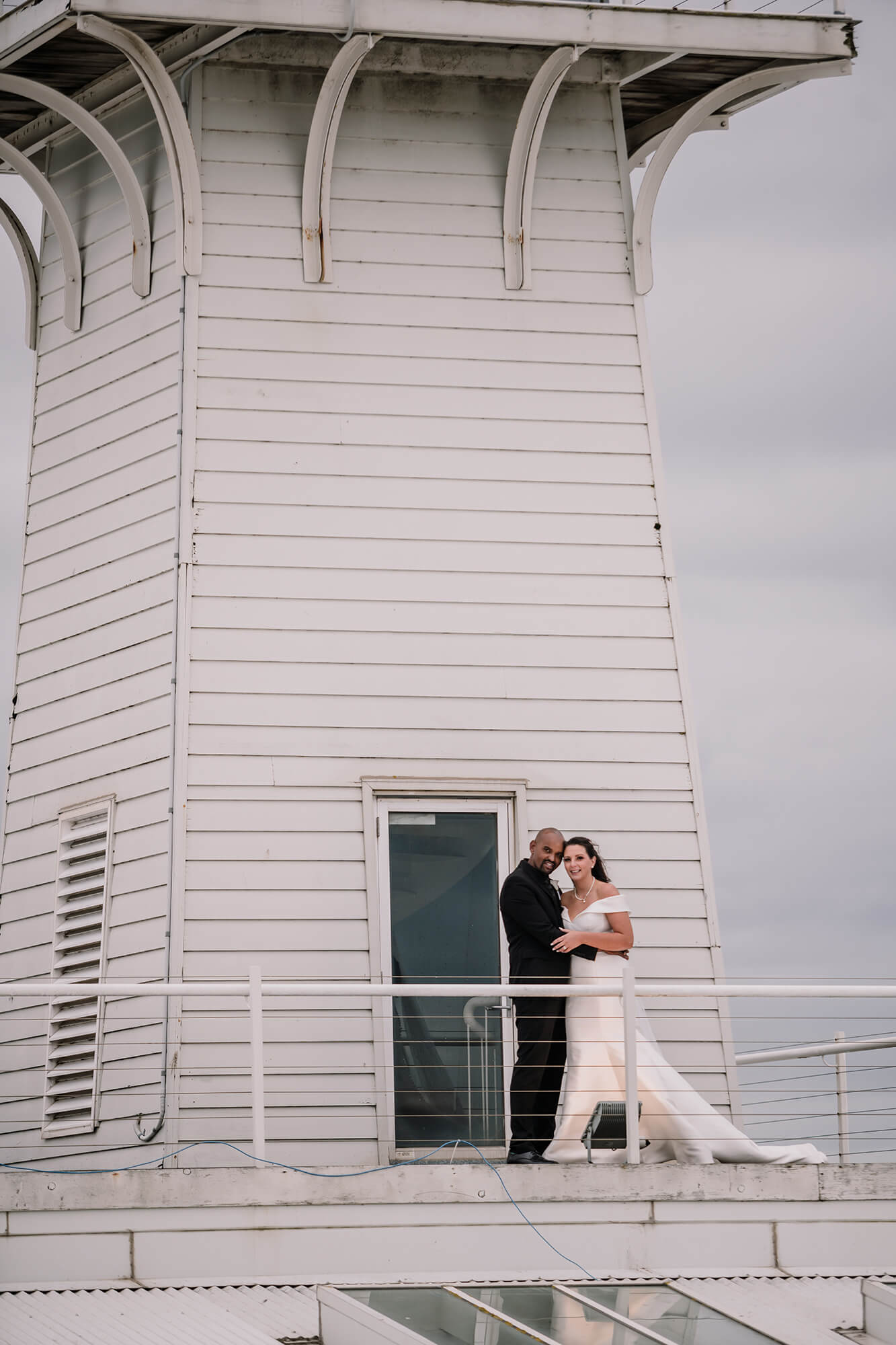 Stunning shot of the bride and groom standing by a lighthouse, captured by Black Avenue Productions