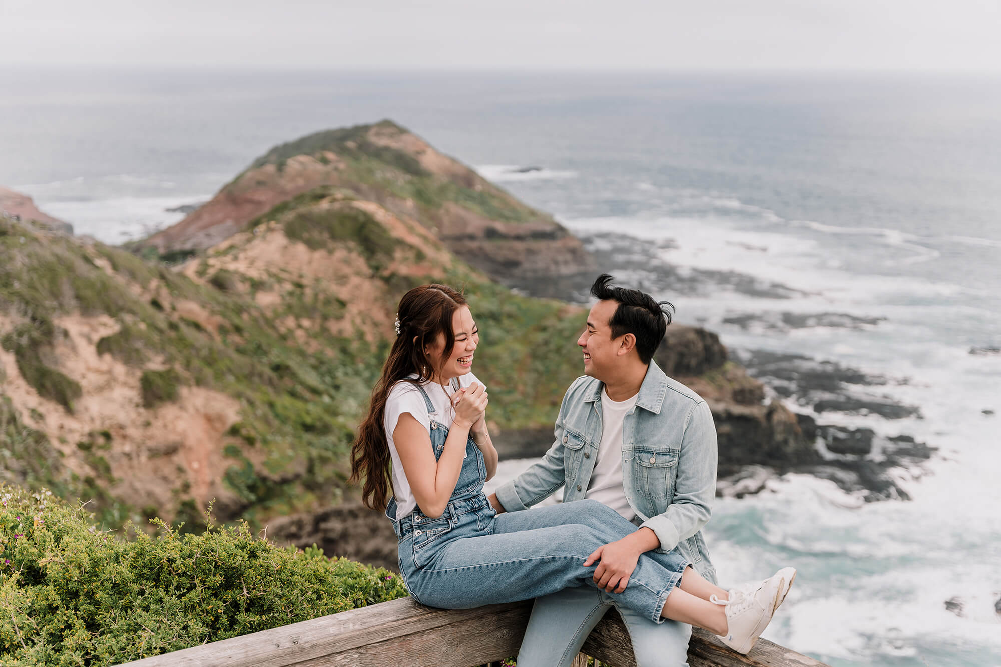 Engagement Photo Ideas, Couple laughing their hearts out with a beautiful view of a hill and the ocean by Black Avenue Productions