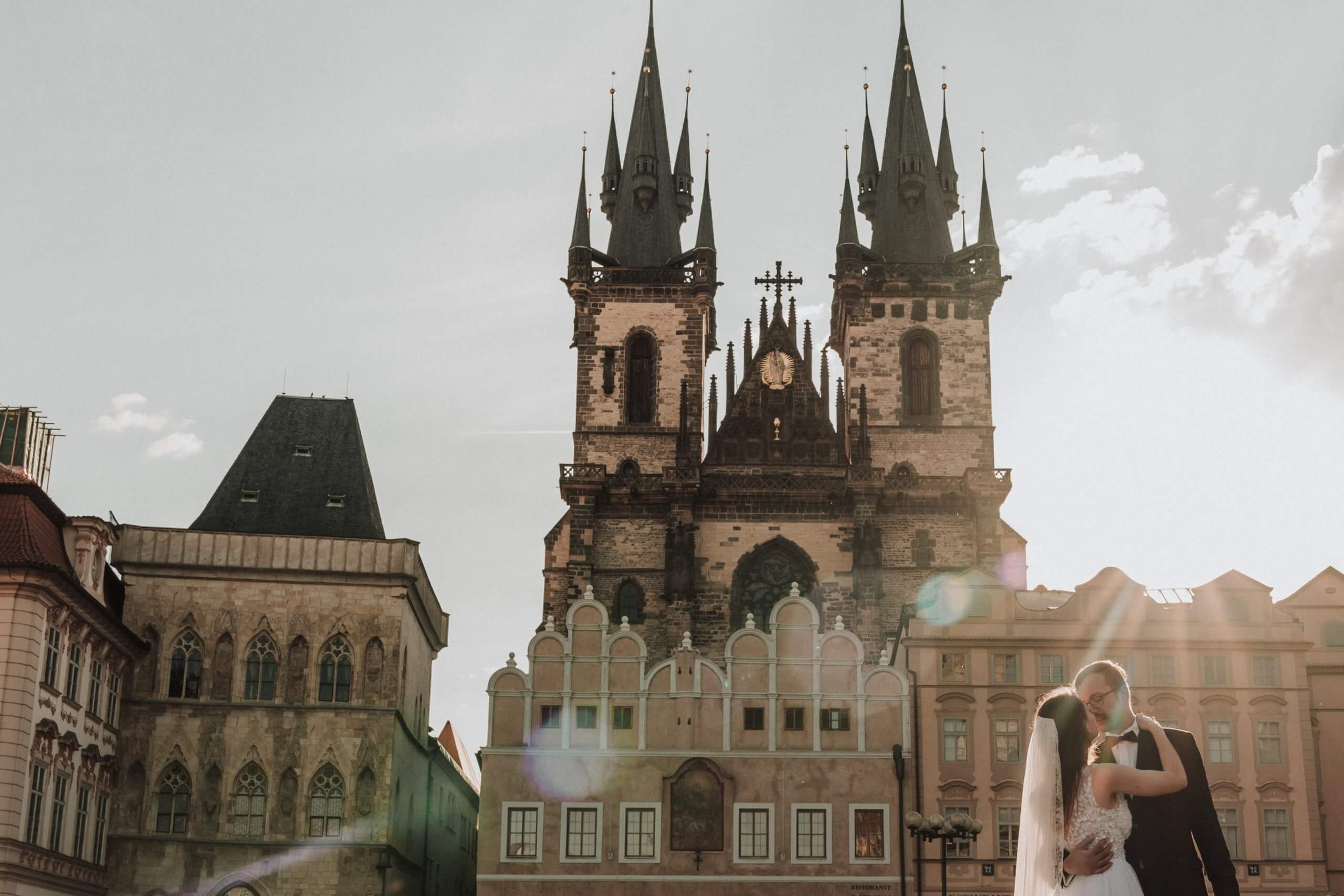 Bride and groom, bathed in golden sunlight in front of the Church of Our Laby before Týn.
