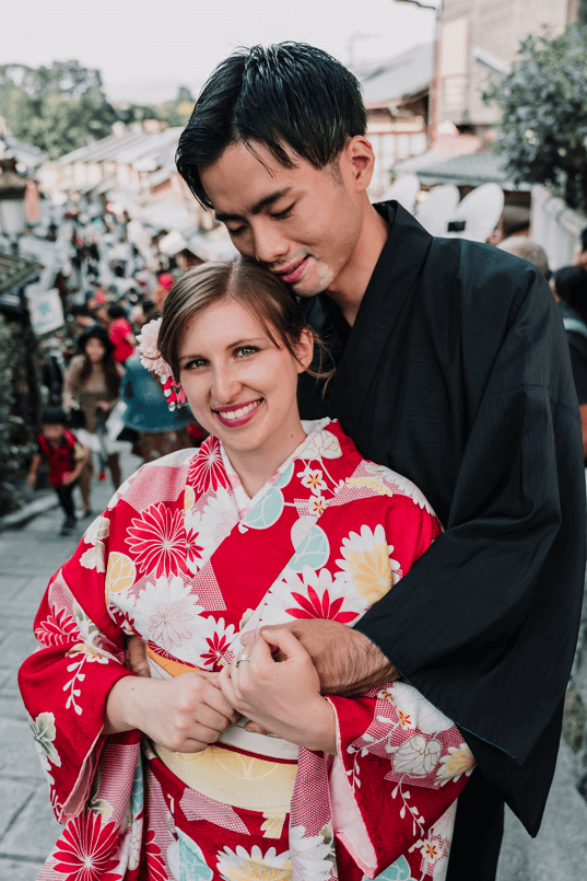 Groom backhugs the bride as she smiles at the camera. The couple is wearing traditional Japanese clothing.