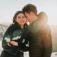 Bride and groom, clad in their winter outfits on top of a snowy mountain at sunrise.