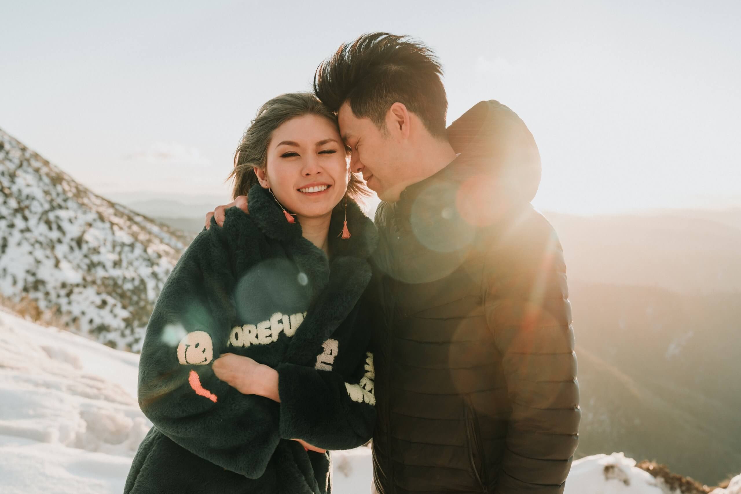 Bride and groom, clad in their winter outfits on top of a snowy mountain at sunrise.