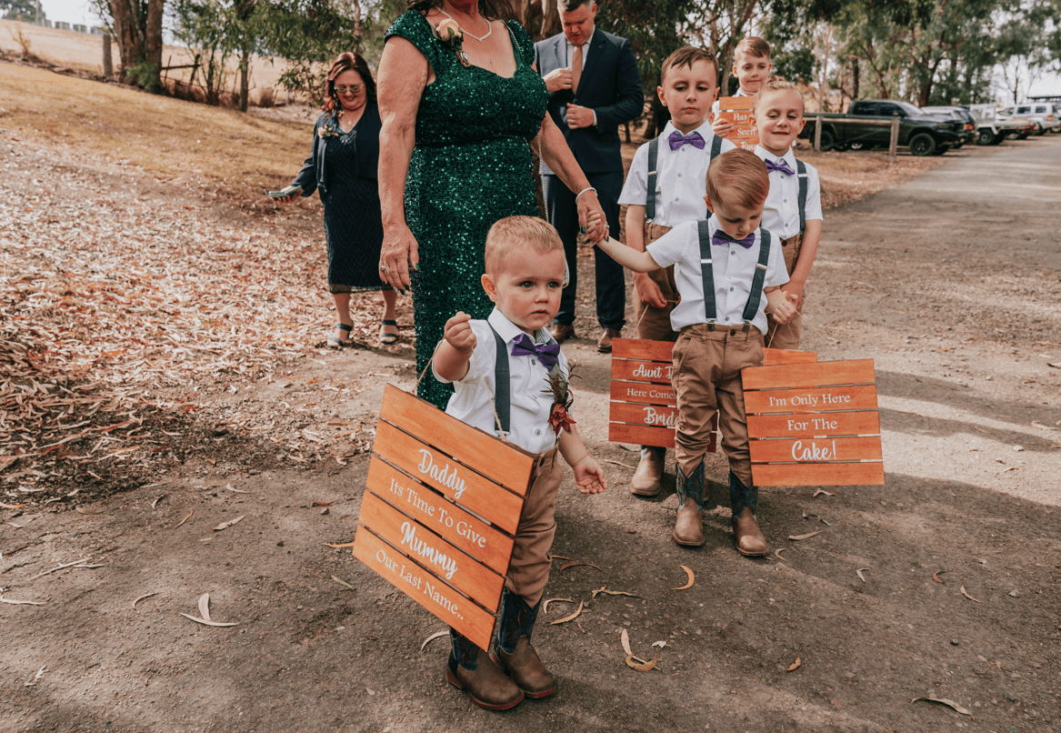 Bride and groom's son getting ready to walk down the aisle while carrying a placard that says "Daddy, it's time to give mummy our last name."