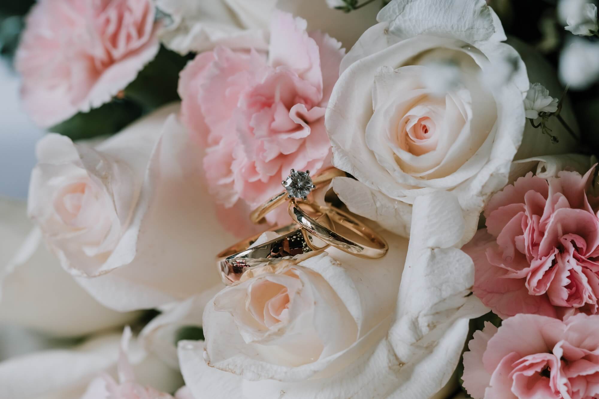 Three gold bands sits prettily on top of white roses and powder pink carnations