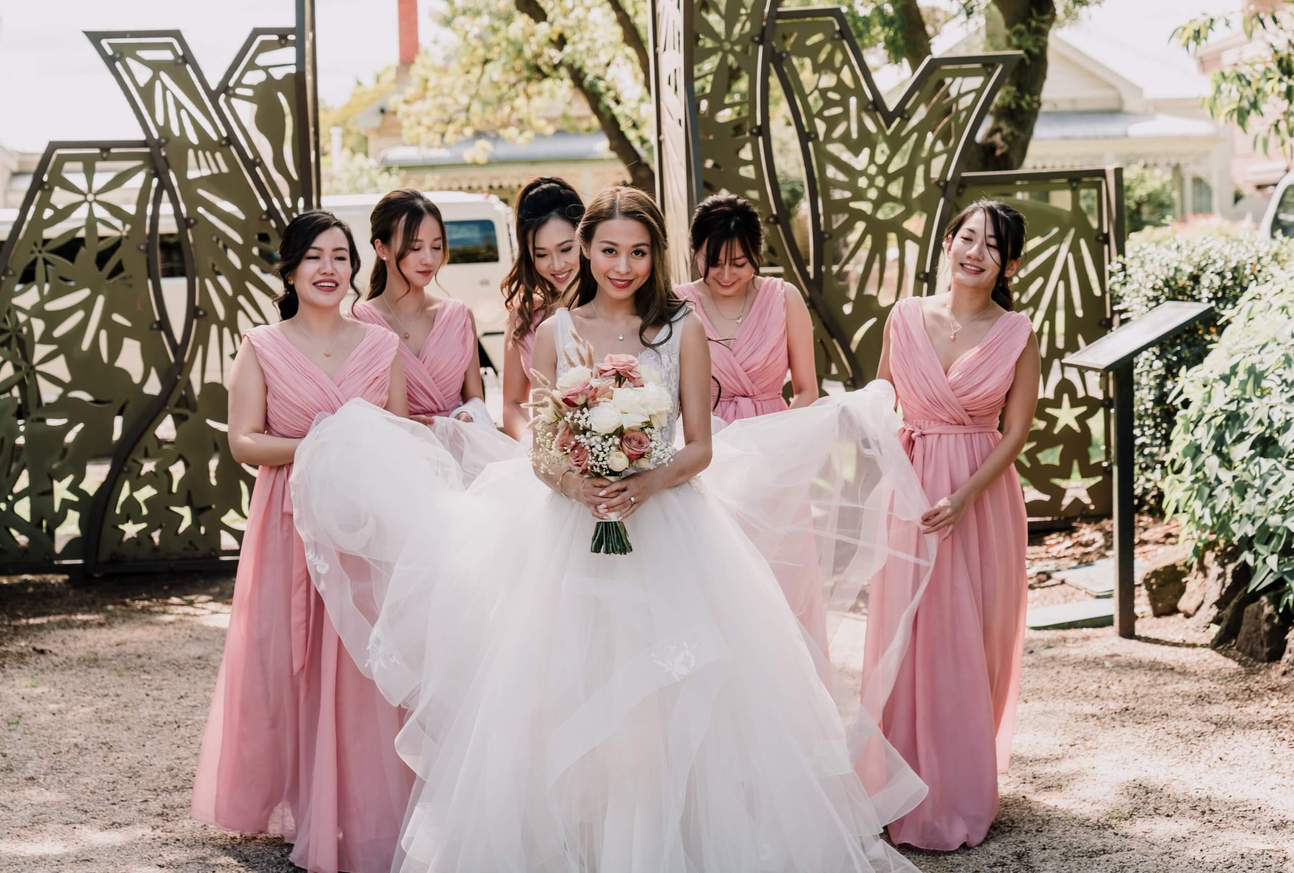 The brides smiles towards the camera while her five bridesmaids hold the trail of her gown