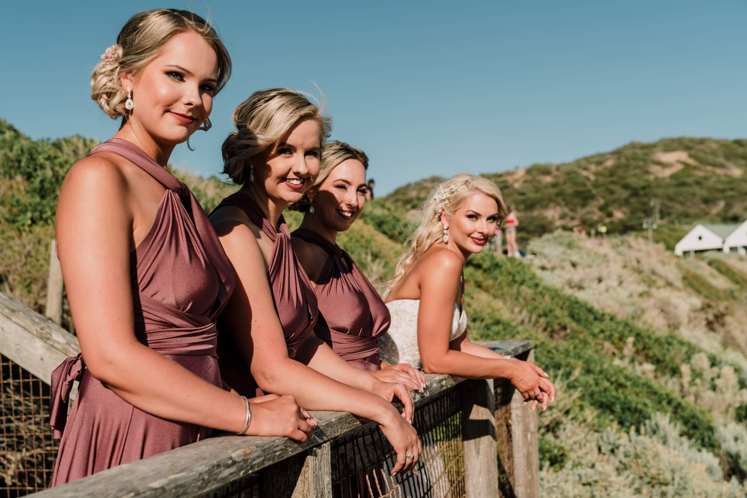 Wind in her hair, bathed by the golden sun, and a beautiful over the shoulder smile, the bride poses for a picture with her bridesmaids