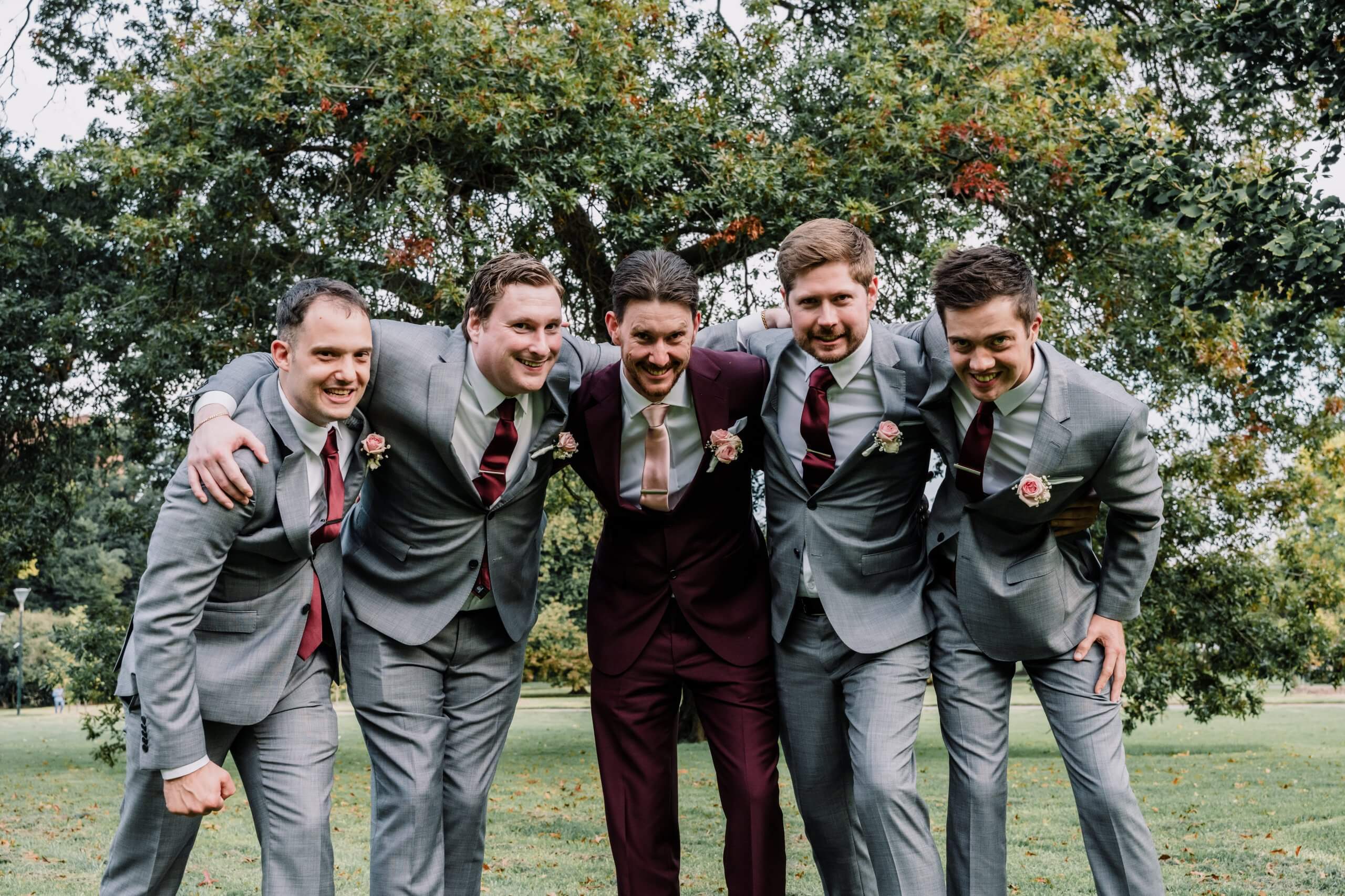 Four groomsmen and a groom with their arms over each other's shoulders, smiles down at the camera.