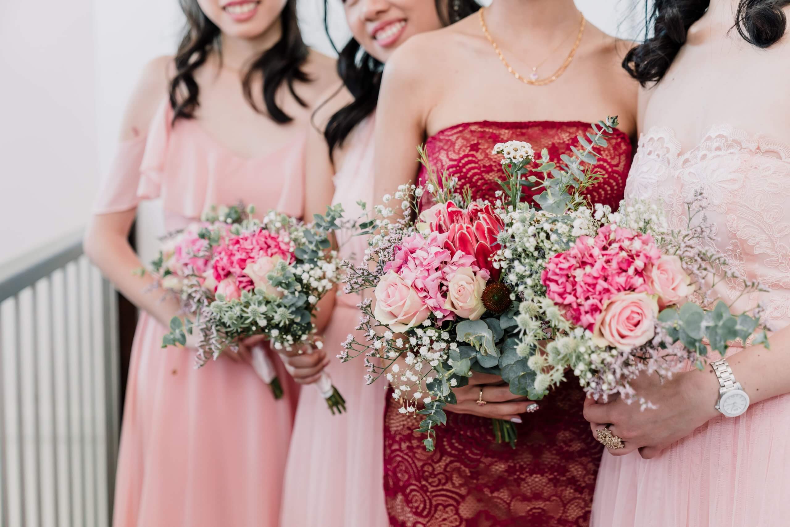 Beautiful bouquet of pink, red, and peach colored roses and carnations held in the hands of the bride and her bridesmaids