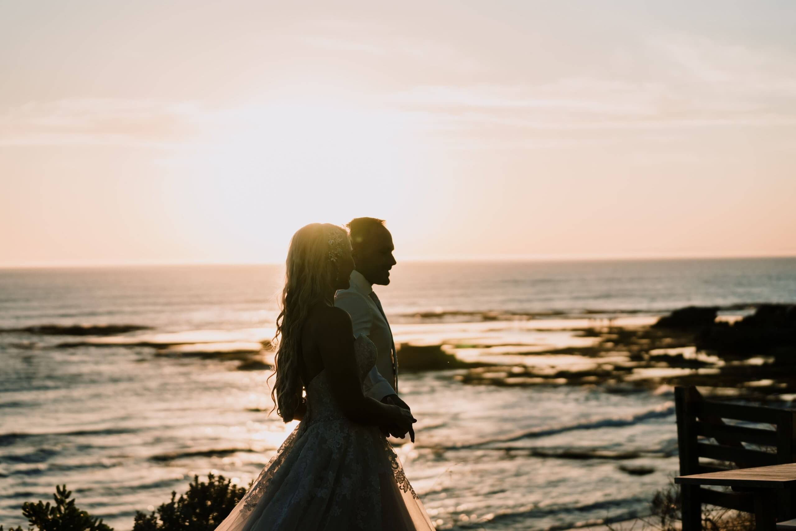 A golden hour photo of the bride and groom as they are walking the shoreline.
