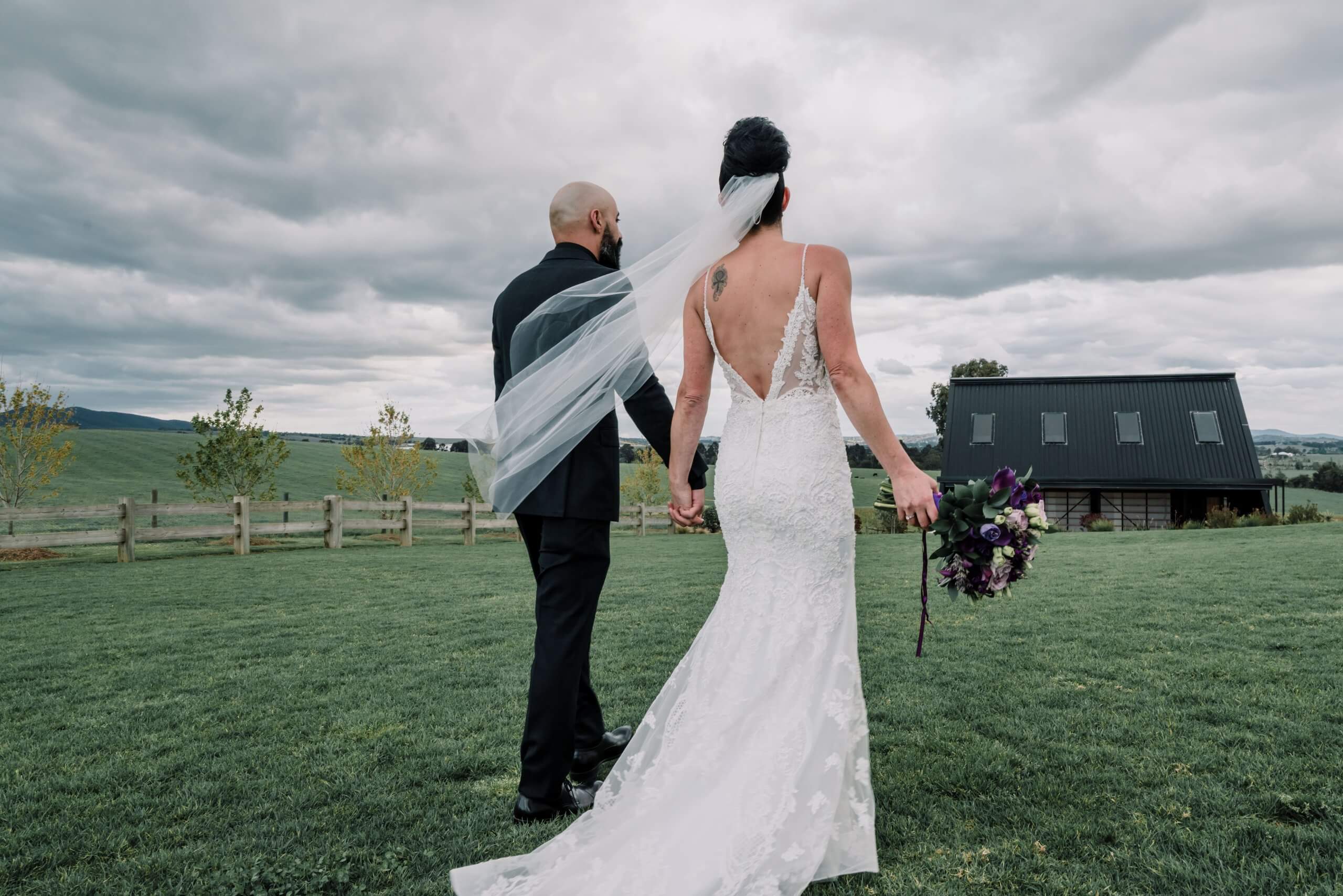 Dramatic back view of the bride and groom walking in the farmlands.