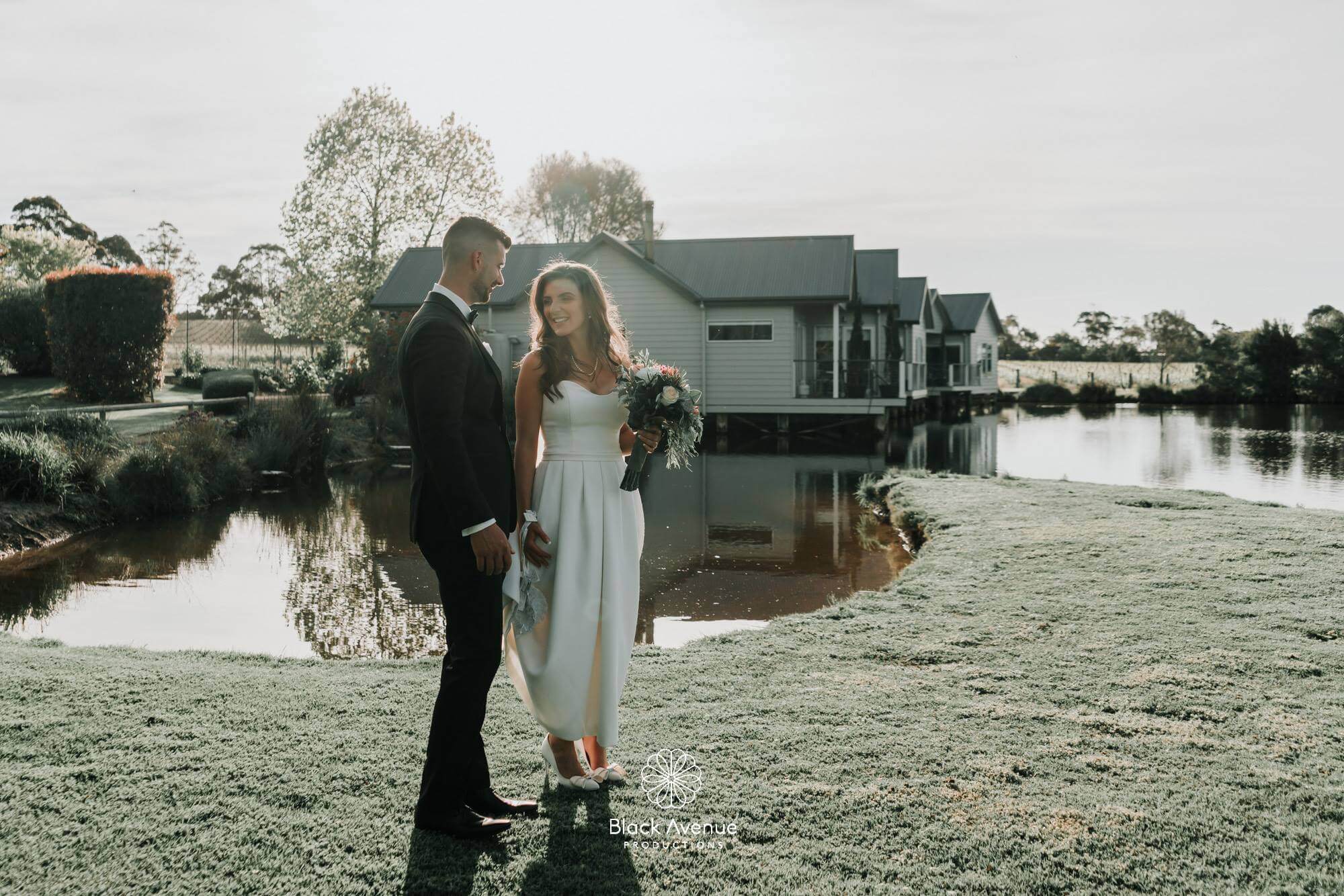 Bathed in the soft and warm light of the setting sun, the bride and groom stands side by side beside a pond